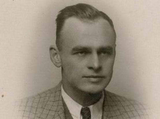A portrait photo of Witold Pilecki. A man in a checked jacket, suit and tie. He has short hair combed to the back.