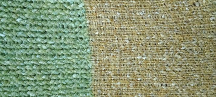 Photo of an excerpt of a loom- knitted blanket, one half light green  and one half in a brownish yellow, each with the occasiobal white thread woven in, knitted in two different stitches. The yellow half (on the right) in a tighter stitch.