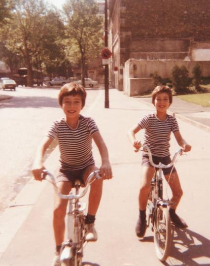 Sur un trottoir parisien, près de Bercy, dans les années 70, deux gamins d'environ neuf ans et habillés à l'identique, sont sur leurs petits vélos pliants. Il fait beau, ils sourient.