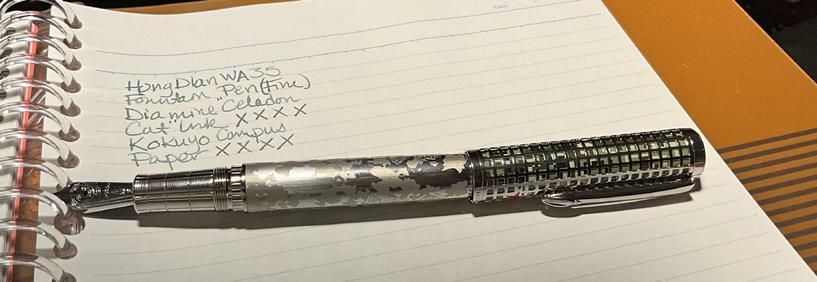 A silver fountain pen on a page of lined paper with handwriting in light blue ink.