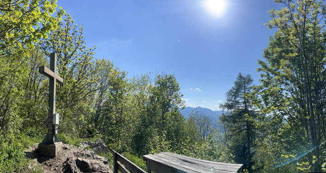Gipfelkreuz mit Tisch im Wald und blauem sonnigen Himmel