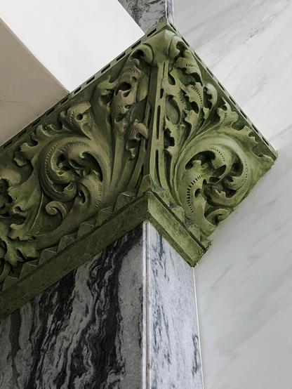 Color photo looking up at a section of intricately modeled plaster crown moulding which has been painted a rich green