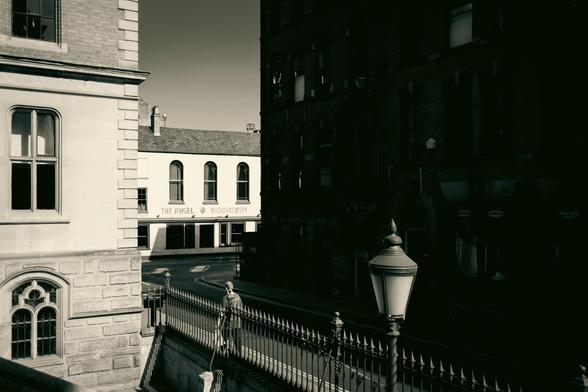 Buildings in sunlight; others in heavy shadows; iron railing and a lamppost.