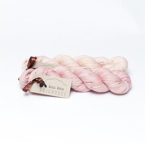 Picture shows two skeins of yarn, one behind the other, in shades of pink with red, yellow and blue speckles.