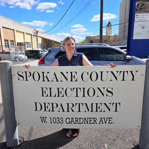 Rebecca Long standing behind the Spokane County Elections sign