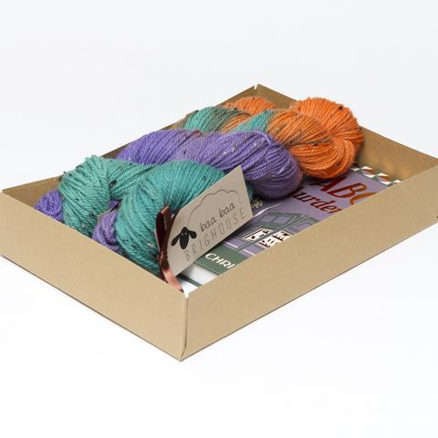 Picture shows an open A4 box containing two skeins of yarn in shades of green, purple and orange. The rest of the box contents is obscured by the sides of the box.