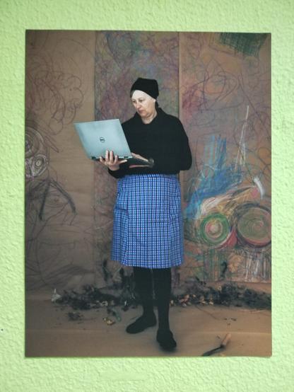 A photograph in the wall that seems vintage. An old lady wearing old style clothes standing with a laptop.
Is the artist performing.