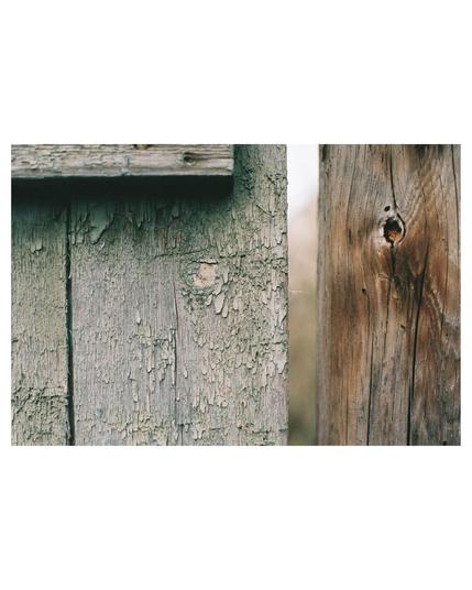 close up of a crumbling blue paint from a wooden fence. A blurry vertical line parts the picture, on the one side the blue fence on the other an old wooden stake