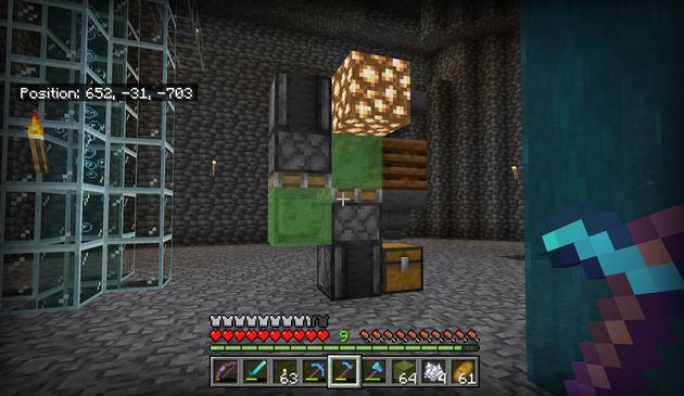 A redstone machine standing in a large hole with deepslate floor and walls. It is a composter with a hopper above and below, depositing bonemeal into a chest after automatically composting moss. A flying machine has been grafted into the side with slime blocks, pistons, and observers that move the whole contraption down when the blocks below it are broken. Two glowstone blocks have been stuck to the top slimeblock to provide some mobile light to the area.