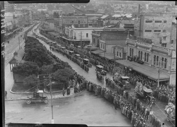Black-and-white photo: State funeral of Prime Minister William Ferguson Massey, Wellington. 1925. Description: An elevated view of the long motorised funeral procession as it passes through Courtney Place. Crowds wearing raincoats line the street. Citation: Crown Studios Ltd: Negatives and prints. Ref: 1/2-192773-F. Alexander Turnbull Library, Wellington, New Zealand. https://natlib.govt.nz/records/23040611