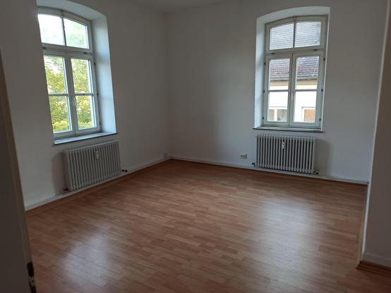Foto von der Tür aus in ein leerstehendes Zimmer mit Parkett und zwei Fenstern.
