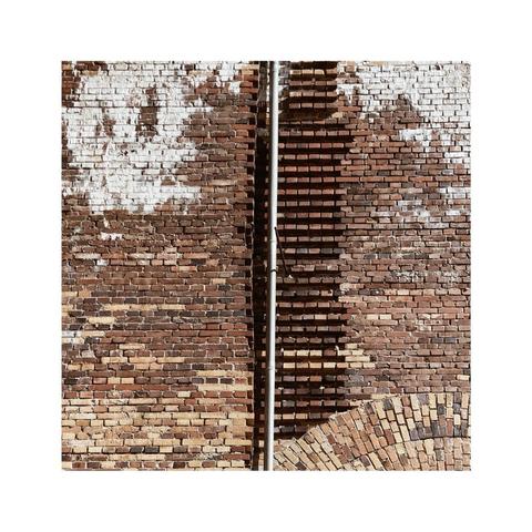 a square image with details of a red brick facade. in the lower right corner there are parts of an old arc, in the center there are brick connectors to a wall that has never been built. also there's a metal gutter dividing the image into two equal halves