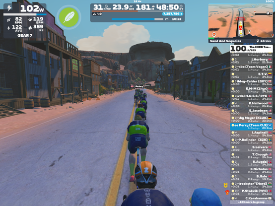 Screenshot from Zwift with riders' avatars in Herd attire rider through the old mining village in Watopia.