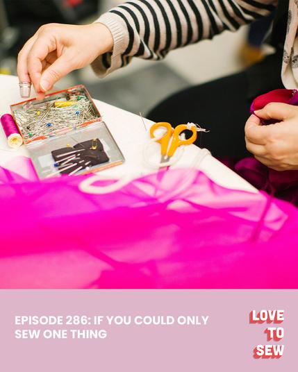 A person wears a thimble and chooses a pin from a box of pins and needles. Bright pink fabric and a pair of scissors lay on the table in front of them.