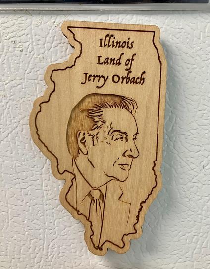 A wooden magnet the shape of Illinois with a laser cut portrait of Jerry Orbach looking dreamily off to the right. It has the words “Illinois land of Jerry Orbach” above the portrait
