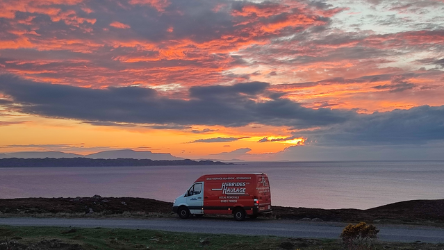 A hebrides haulage van parked in a scenic place against the isles of Raasay and Skye in the background and an orange, evening sky.