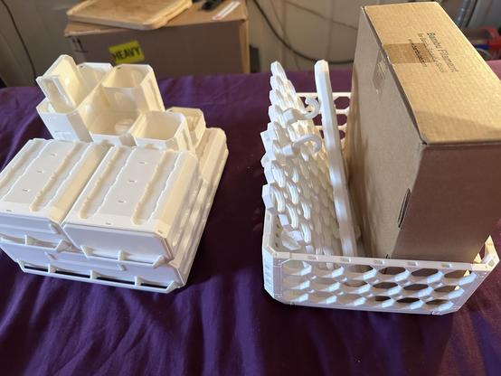 A pair of white plastic boxes : one a rectangular open-basket design, the other a sort of tiny plastic chest of drawers, with Gridfinity bins somehow assembled to it. The basket is full of printed parts, awaiting assembly.