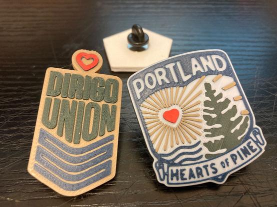 Three pins. One says Dirigo Union, one says Portland Hearts of Pine, one is turned upside down.