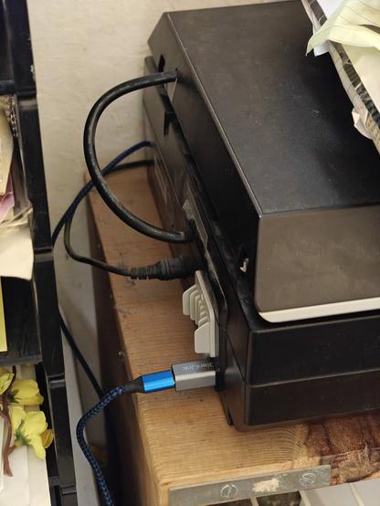 A thin blue cable fitted with a much larger silver adapter in is plugged into the back of a computer peripheral.