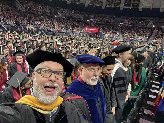 A smiling bearded man in a robe and wizard hat with a thousand other people in robes and wizard hats