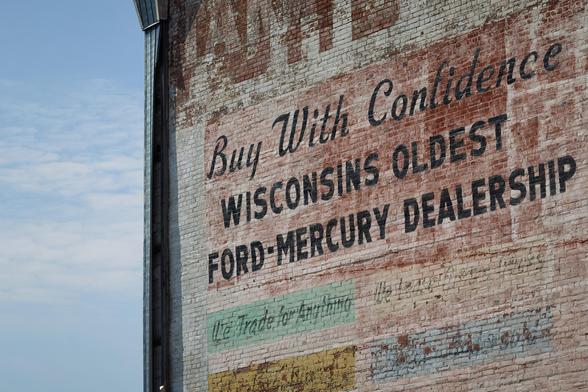 Photograph of a brick wall with the words "Buy With Confidence Wisconsin's Oldest Ford Mercury Dealership" painted on it.