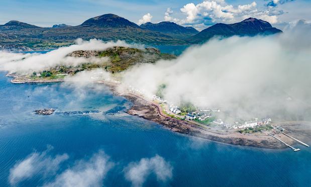 Fog lingers over a peninsula. Blue sea below.