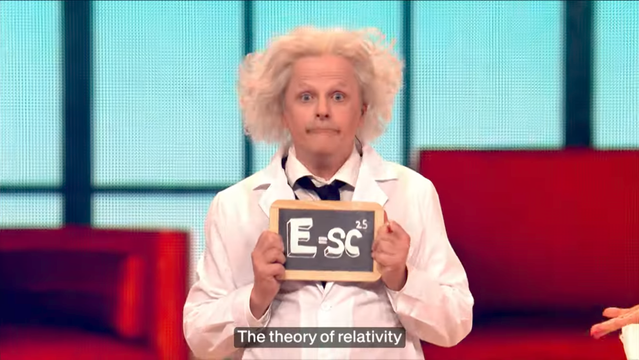 Actor made to look a bit like Albert Einstein, holding up a chalk board with the writing E equals sc to the power of 25