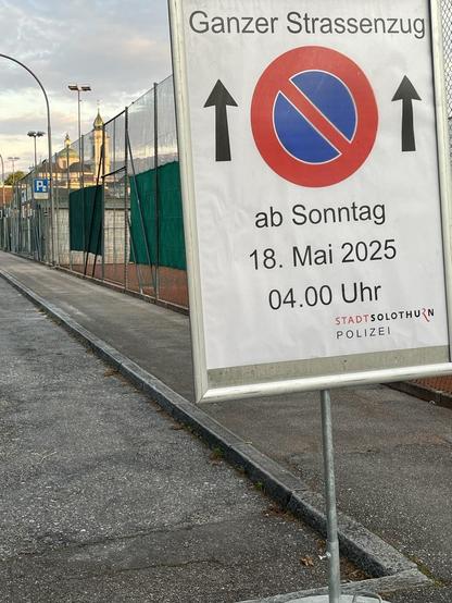Ein großes Schild an der Strasse mit der für Sonntag angekündigten Strassensperrung, im Hintergrund leuchtet die Kathedrale in der Sonne.