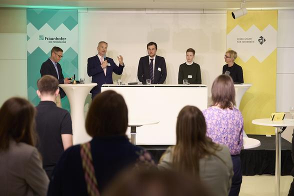 Markus Reichel spricht, mit ihm auf der Bühne Boris Otto, Johannes Schätzl, Rebecca Lenhard und Christine Regitz, sie stehen zwischen Bannern für Fraunhofer IUK und GI