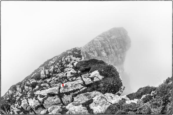 Schwarzweissfotografie mit Selektivfarbe Rot einer rot markierten Bergwegs im Nebel.