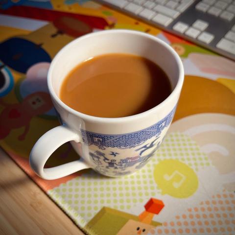 A mug of tea on a colourful Katamari desk mat.