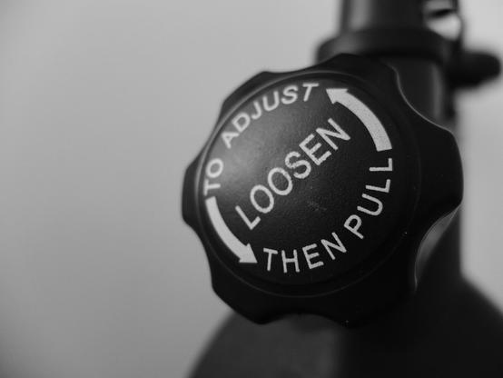 Close-up of a black adjustment knob with white text and arrows, instructing: "TO ADJUST LOOSEN THEN PULL."