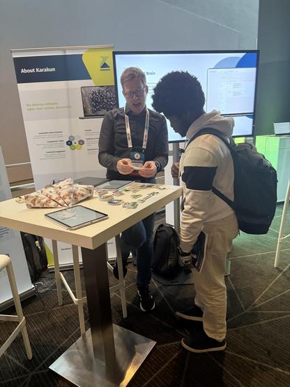 Visitor at the Karakun booth at JCON in Cologne talking to Karakun expert Andreas. They are standing at the table and discussing about stickers.