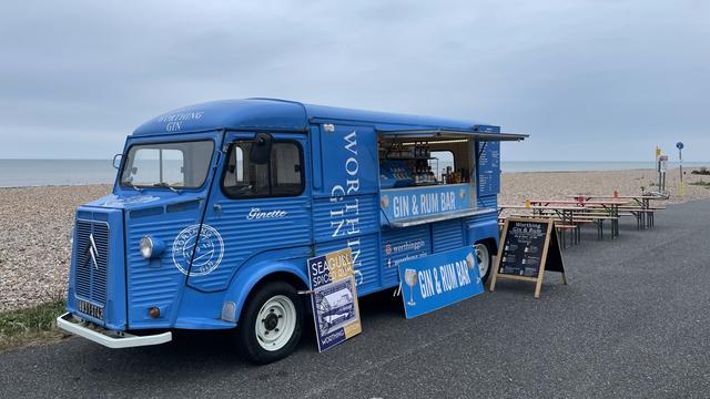 The Worthing Gin van open for business. In the background is a cream pebble beach, grey sky and steel-blue sea