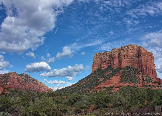 Sedona’s great wide open of desert beauty and skies so blue is captured with this breathtaking view of a summer sky with white clouds that drift over Courthouse Butte and the red rock formations in the distance. Courthouse Butte is an impressive mass of sedimentary rock that rises to nearly a 1,000 feet in the air. It is easy for the soul to make a spiritual connection to the elements of earth and sky is one listens to the song in stone and wind.