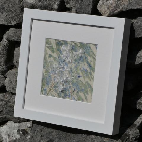 The same artwork (Rose Bay Willow Herb number 2) framed in white and resting against a stone wall