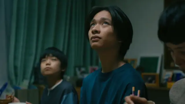 A young man next to a couple of other people at a dining table, looks up, worriedly