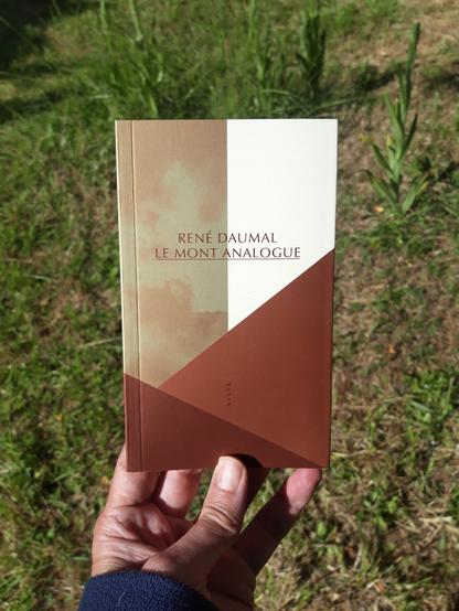 A hand holds a copy of a small book entitled "Le Mont Analogue" by René Daumal.
