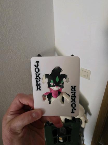 a picture of a 3d printed version of the "joker stencil" joker from balatro. behind the stencil cutout, there's a meowscarada plushie