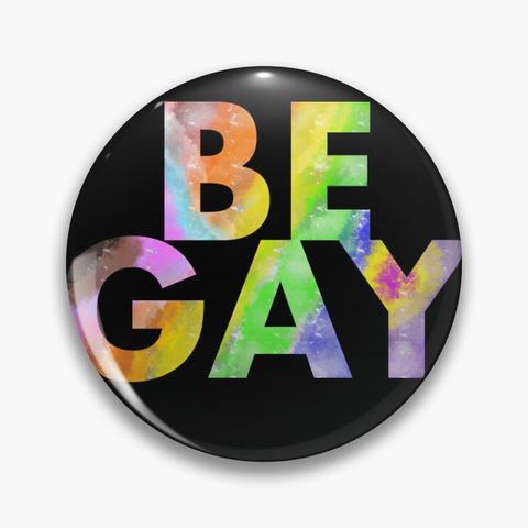 a round button/pin in black that features large letters in rainbow colors, showing all progress pride colors. the text says BE GAY