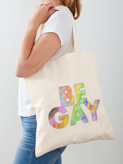 a tote bag that features large letters in rainbow colors, showing all progress pride colors. the text says BE GAY