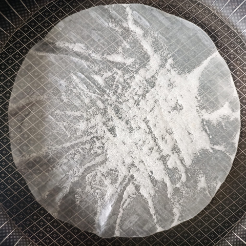 In einer Pfanne ein rundes Blatt Reispapier, das sich gerade weiß färbt