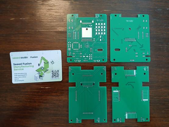 Photo de 4 PCB de couleur verte, 2 designs présentés recto/verso. Le PCB du haut est le plus dense, on y voit beaucoup de traces pour des composants montés en surface. Celui du bas est beaucoup plus "léger", il doit ne devra avoir que des capteurs et quelques capacités, ainsi qu'un connecteur de câble en nappe. Sur la gauche, une carte de visite "seeedstudio".