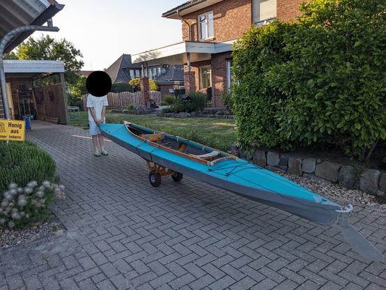 Auf dem Foto sieht man das aufgebauten Faltboot auf einem Bootswagen liegen. Mein Patenkind schiebt das Boot über die Hofeinfahrt.