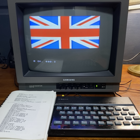 a ZX Spectrum connected to a TV showing the union flag. The basic manual is open on the page with the code.