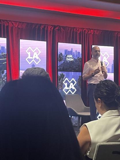 A man standing on stage at a conference. Sorry I’m so bad at writing alt text.