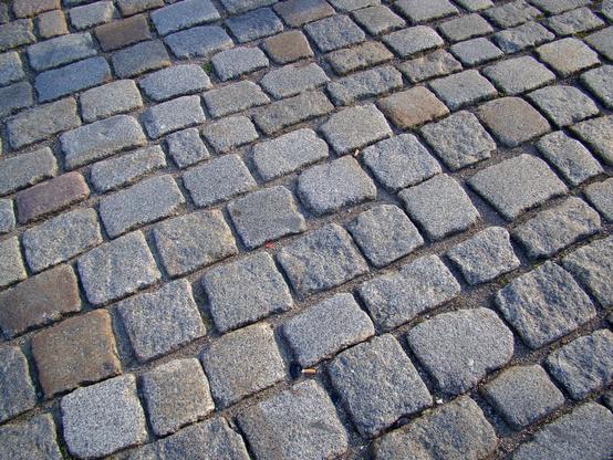 Detailaufnahme eines Gehwegs aus Pflastersteinen. Die Steine haben verschiedene Farben.