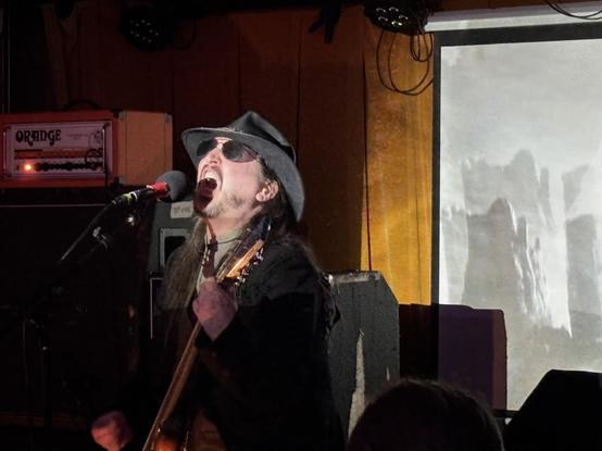 Man in black, leather cowboy in shades, playing guitar and howling into the mic.