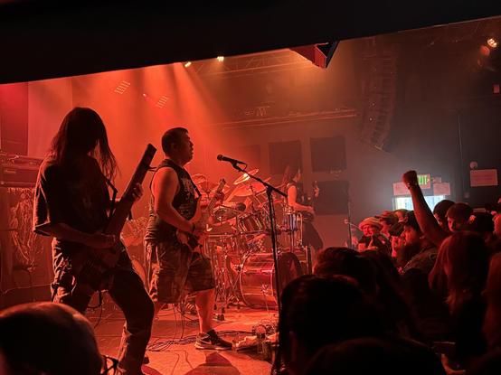 View from stage right, red lights, the band wearing shorts and playing headless guitars. Got some of the audience in the shot too, complete with raised fist!