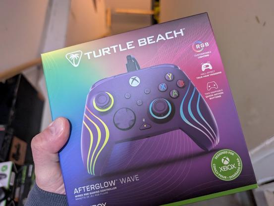 Multicoloured rainbow box showing the Turtle Beach Afterglow Wave Xbox Wired Game Controller. The controller itself is purple with glowing LED waves along each hand grip and around both thumbsticks.